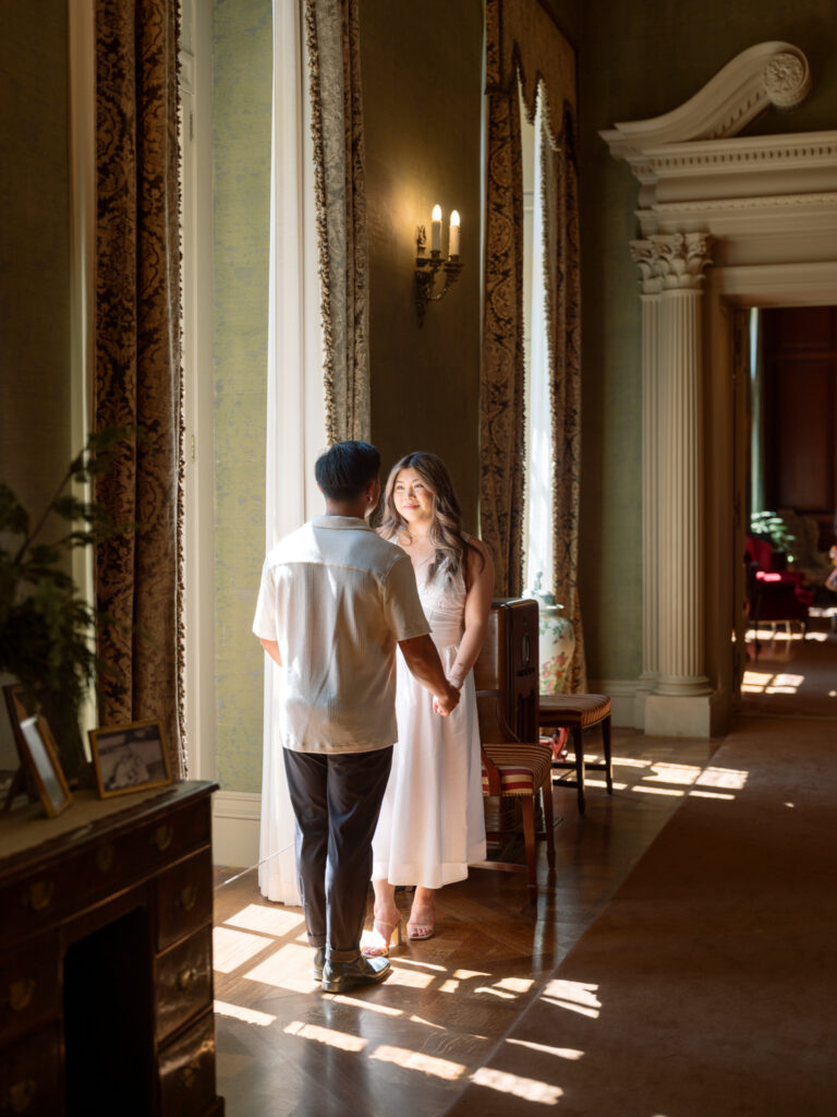 Engaged couple hold hands and look at each other inside Filoli main house