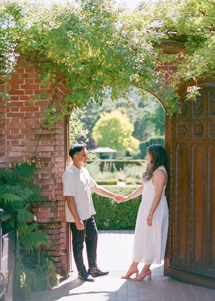 Fiances at their Filoli engagement session against red brick and garden