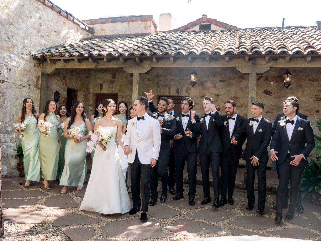 Bride and groom walk with their wedding party in front of the inner courtyard at Holman Ranch