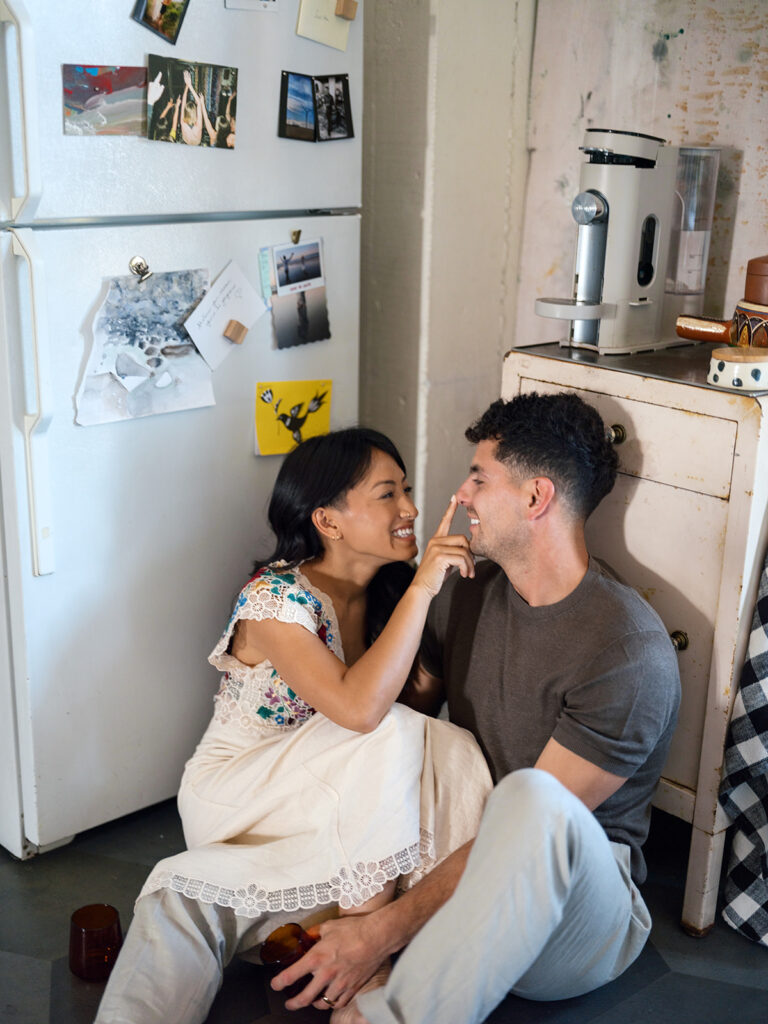 Newly engaged couple laugh together on the floor of their loft kitchen during a Bay Area engagement photo session