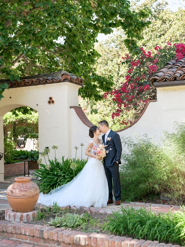 Bride and groom pose amongst the bougainvilleas and lush greenery at the Allied Arts Guild, an ideal Bay Area wedding venue for those dreaming of a garden party wedding