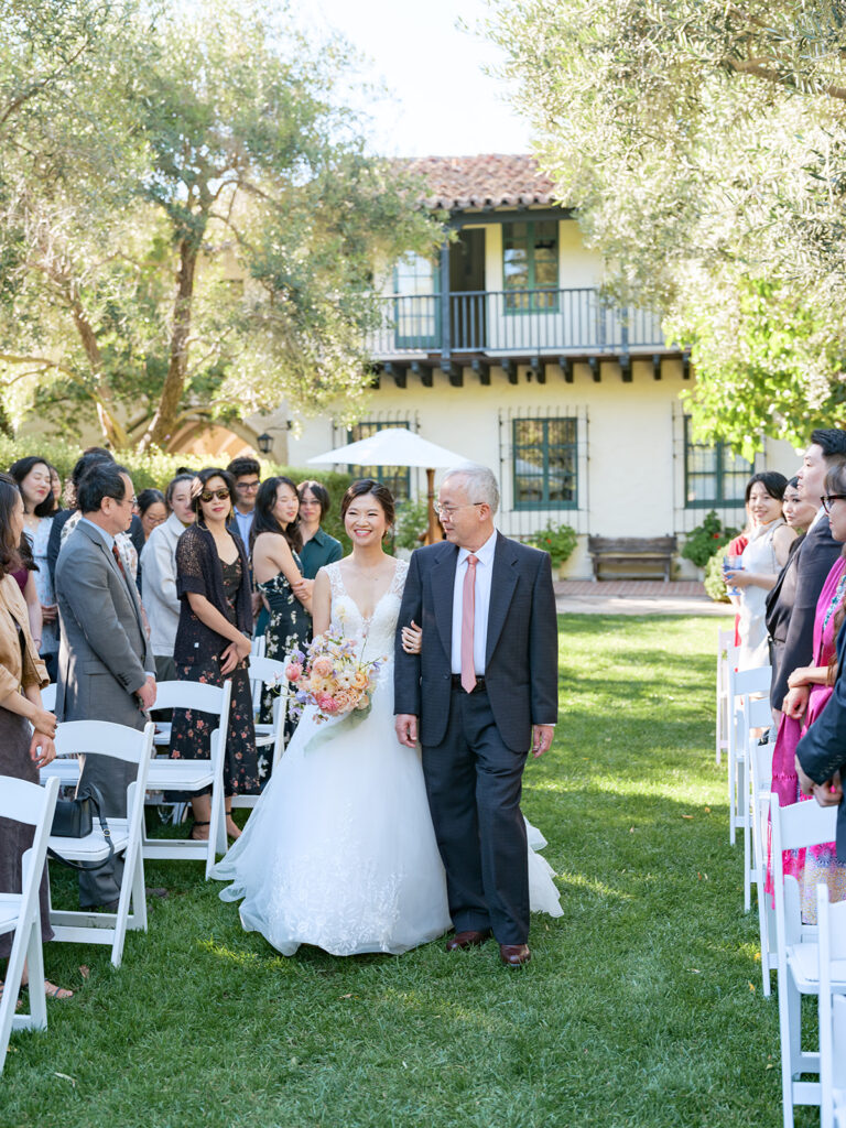 Bride and her father walk down the aisle during wedding processional at Bay Area wedding venue featuring Spanish architecture and garden setting