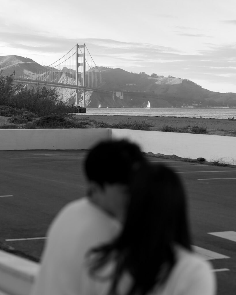 A view of the Golden Gate Bridge as an engaged couple leans in to each other during their San Francisco engagement photo session
