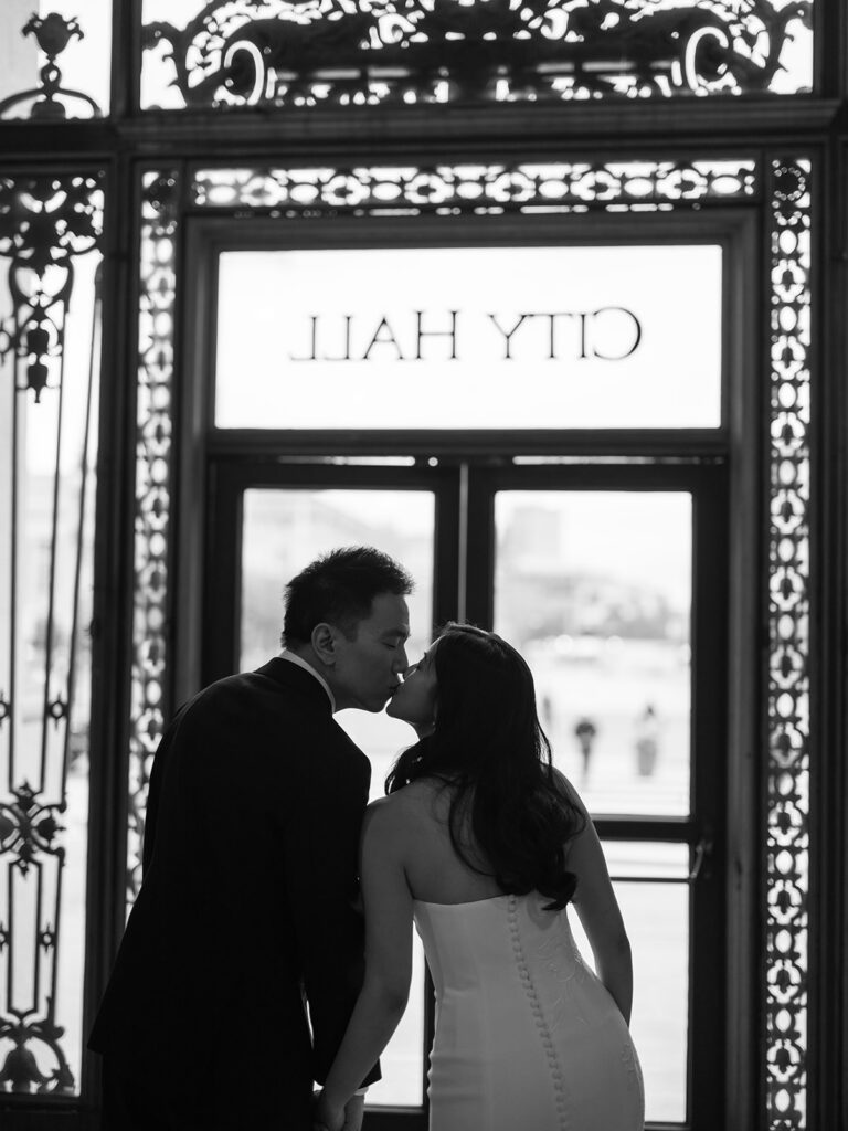 bride and groom leaning in for a kiss in front of the doors of san francisco city hall