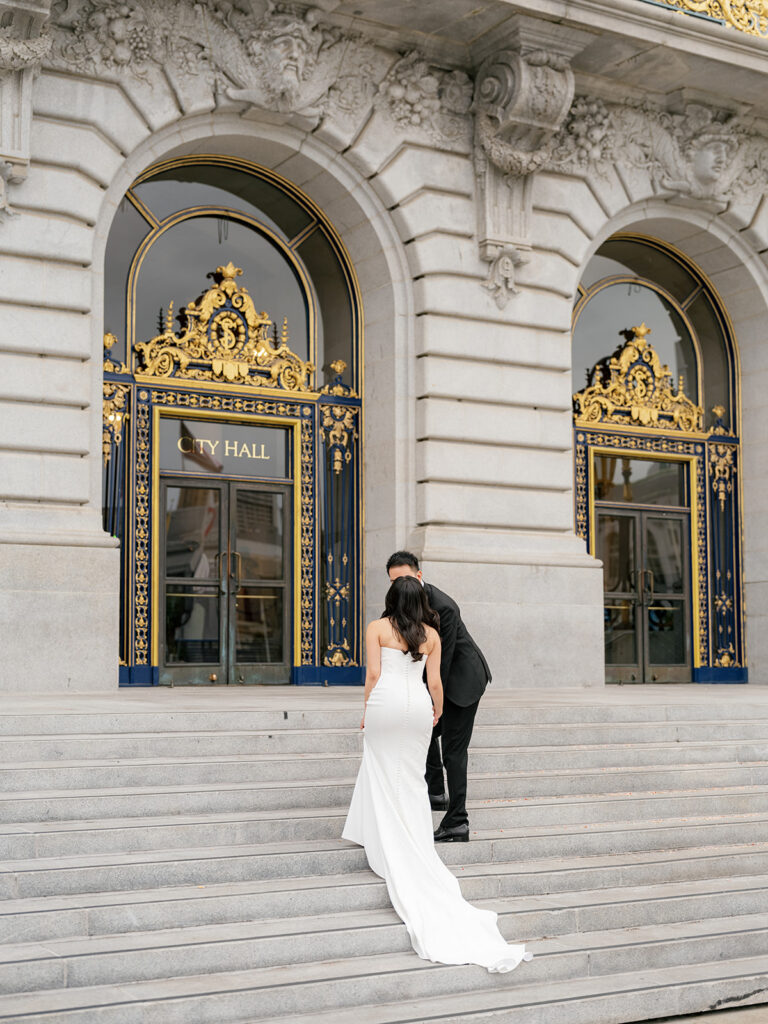 bride and groom kiss on the steps leading up to the San Francisco City Hall building, ahead of their wedding