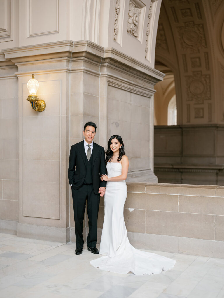 bride and groom posing for a classic wedding portrait looking at the camera at San Francisco City Hall fourth floor balcony