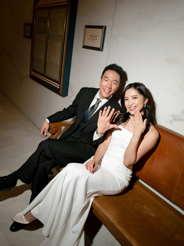 flash photo of bride and groom sitting in the city hall showing off their wedding bands as newlyweds