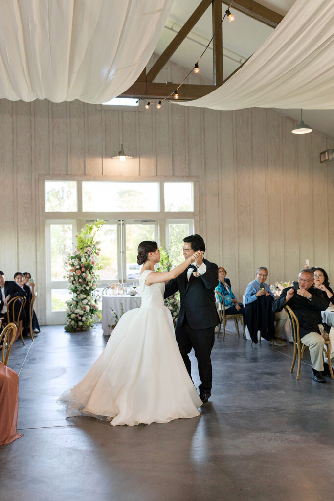 Bride and groom sharing their first dance inside The Barn at Harrow Cellars, warm chandelier light and white draped ceiling above — Sonoma wedding photographer
