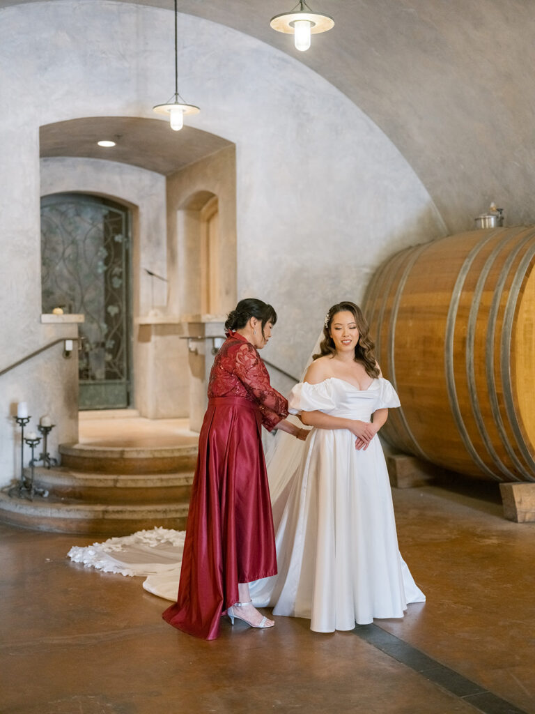 Bride in off-shoulder white gown being helped by her mother inside Viansa Winery's wine cave — Sonoma wedding photography by sustudio