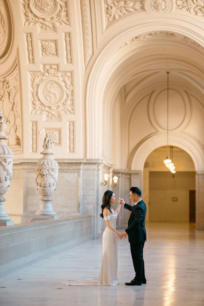 Groom spinning bride in the colonnade hallway at San Francisco City Hall, stone urn and ornate arched ceiling behind them — San Francisco City Hall wedding photographer