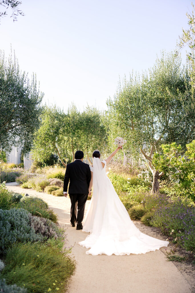 Bride raising her bouquet as she and her groom walk through The Barn at Harrow Cellars' olive tree garden — Sonoma wedding photography by sustudio