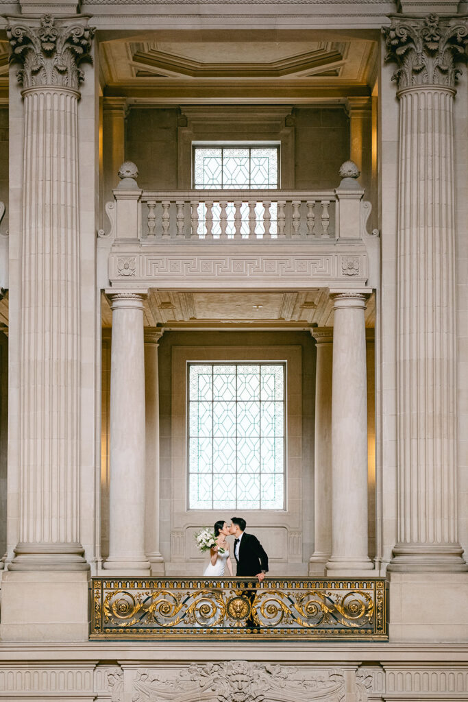 Couple kissing on upper floor of San Francisco City Hall framed by ornate stone pillars
