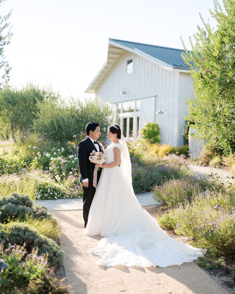 Bride and groom portrait in the wildflower garden at The Barn at Harrow Cellars, Sonoma, white barn facade behind them at golden hour