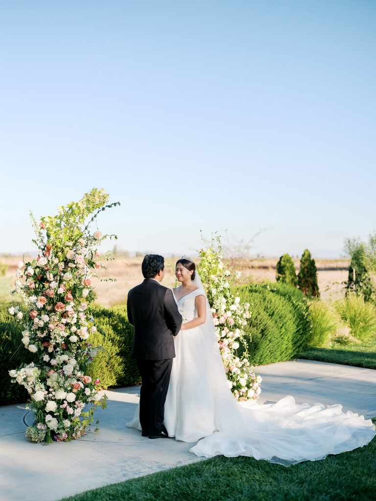 Bride laughing with groom at The Barn at Harrow Cellars' floral arch, Sonoma vineyard and golden hills stretching behind them