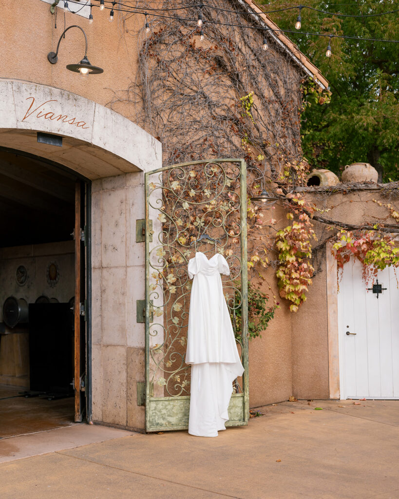 Wedding dress hanging on the ornate entrance gate at Viansa Winery in Sonoma, ivy-covered stone wall in the background