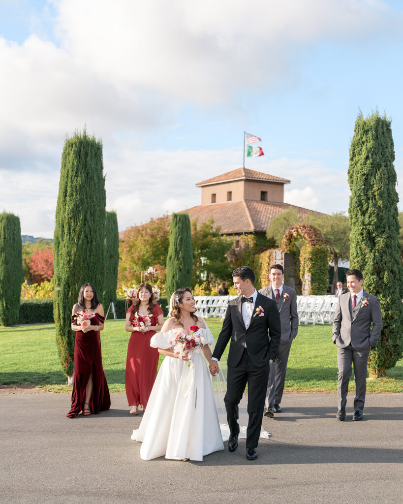 Bride and groom walking with their wedding party at Viansa Winery, cypress trees and the Viansa tower framing the scene